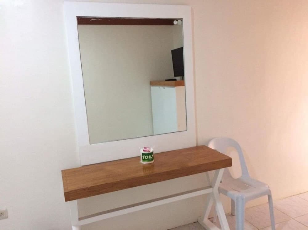 A cozy hotel room corner features a wooden vanity table with a white-framed mirror above it, accompanied by a plastic chair, ideal for travelers seeking simplicity and functionality in their accommodations.