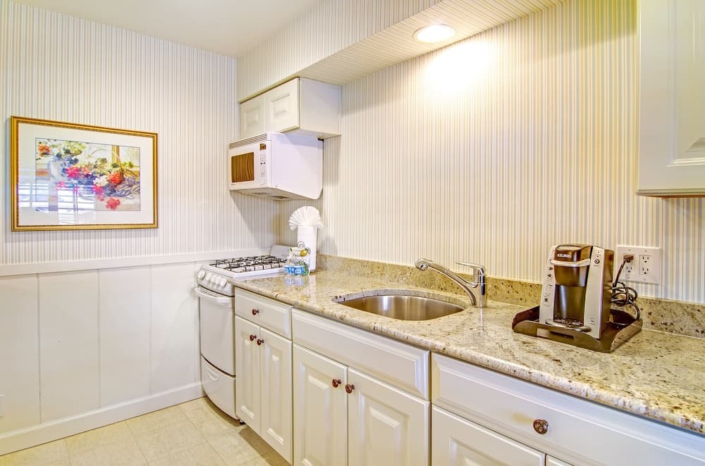 A cozy kitchenette with striped wallpaper, white cabinetry, granite countertops, and modern appliances creates a warm and inviting atmosphere ideal for travelers seeking a homey cooking experience during their stay.