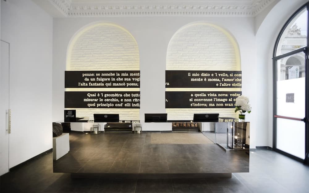 A modern art gallery space features illuminated brick arches with Italian text projections, sleek furniture, and a minimalist design, ideal for cultural exploration and photography.