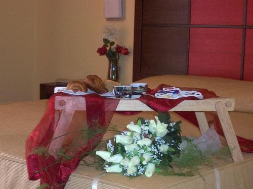 A cozy hotel room setup features a breakfast tray with pastries and coffee on a wooden table draped in red fabric, complemented by fresh flowers, creating an inviting and romantic atmosphere ideal for a special getaway.