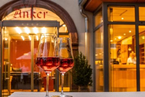 Two glasses of rosé wine gleam on a table outside a warmly lit restaurant with an inviting "Anker" sign, perfect for travelers seeking a cozy evening dining experience.