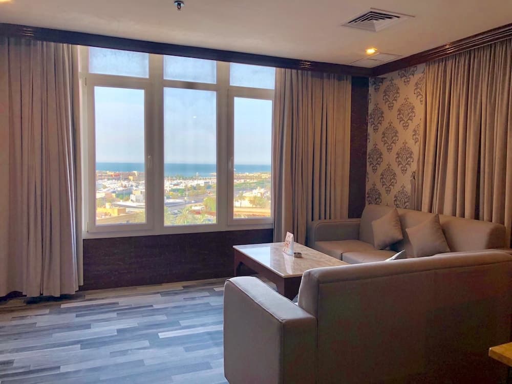 A cozy hotel suite with plush seating and elegant decor offers a serene view of the sea through large windows, ideal for travelers seeking relaxation and comfort.