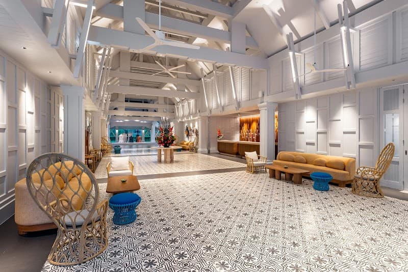 A spacious, brightly lit hotel lobby in SAii Laguna Phuket features modern decor with patterned flooring, cozy seating areas, and elegant white architecture, ideal for travelers seeking a luxurious and relaxing atmosphere.