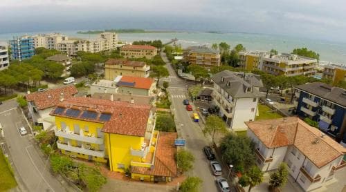An aerial view captures a vibrant coastal town with colorful buildings, parked cars, and a serene sea backdrop, ideal for travelers seeking a relaxing seaside getaway.