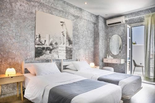 A cozy hotel room with textured walls, a large artwork, two neatly made beds, and a balcony view, ideal for travelers seeking comfort and style in their accommodations.