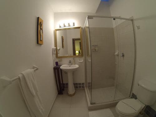 A cozy hotel bathroom features a glass-enclosed shower, pedestal sink, gold-framed mirror, and soft lighting, creating a clean and inviting atmosphere ideal for travelers seeking comfort.
