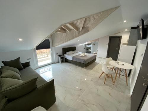 A cozy attic apartment features a modern design with marble flooring, a sleek bed, a small dining area, and a balcony view, ideal for travelers seeking a stylish and comfortable urban retreat.