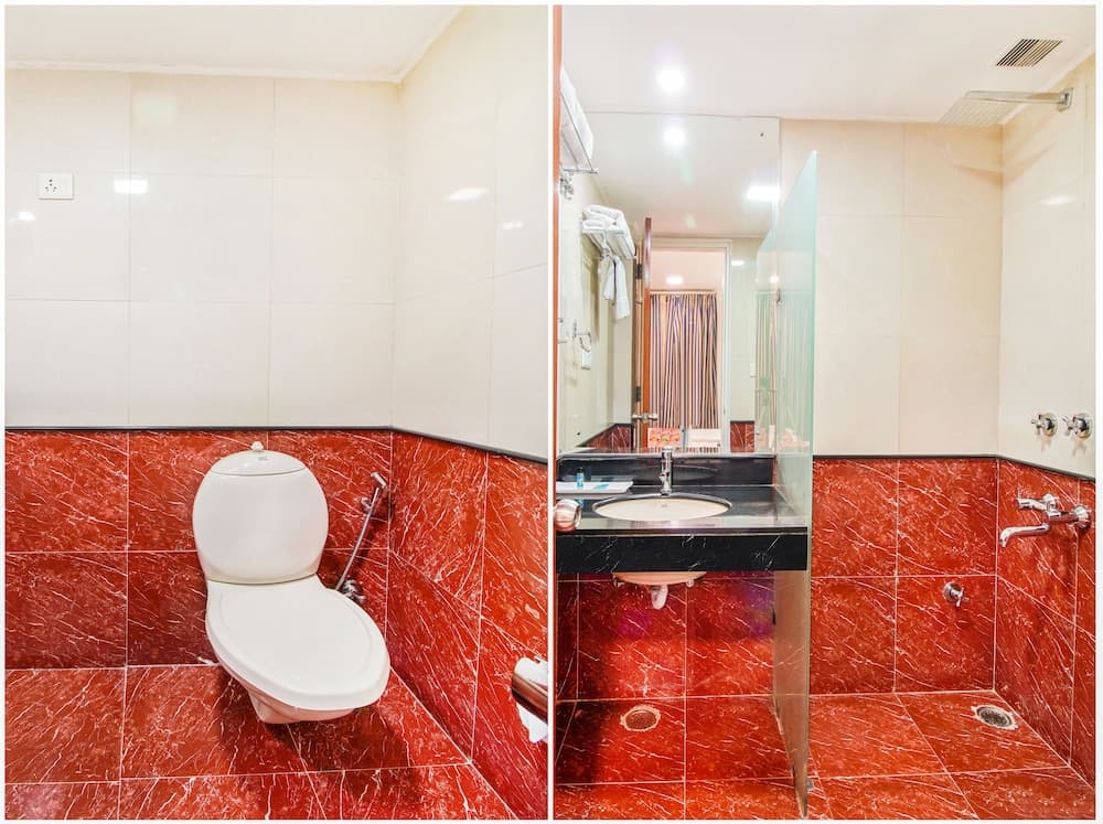 A modern bathroom with striking red marble tiles features a clean toilet, sleek sink, and glass-enclosed shower area, ideal for travelers seeking comfort and style in their accommodations.