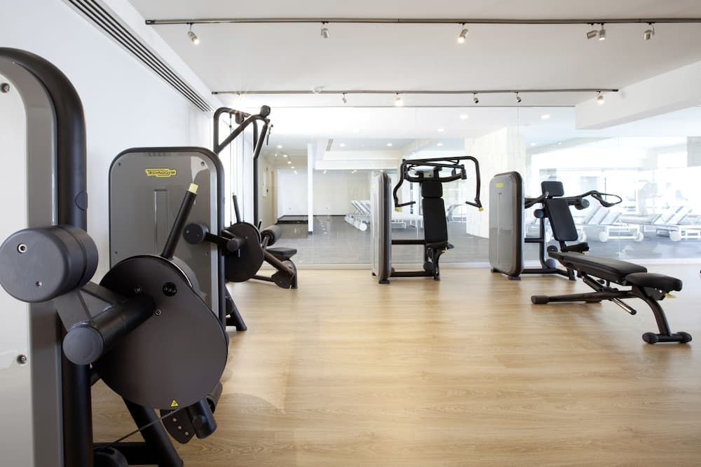 A modern gym with sleek Technogym equipment on wooden flooring, featuring a bright, airy atmosphere ideal for fitness enthusiasts seeking a clean and spacious workout environment.