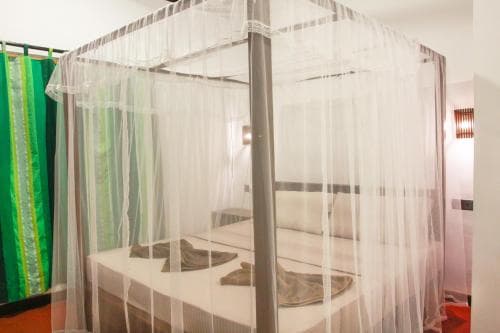 A cozy bedroom features a bed enveloped in a mosquito net, vibrant green curtains, and warm lighting, creating an inviting atmosphere ideal for travelers seeking comfort and protection in tropical destinations.
