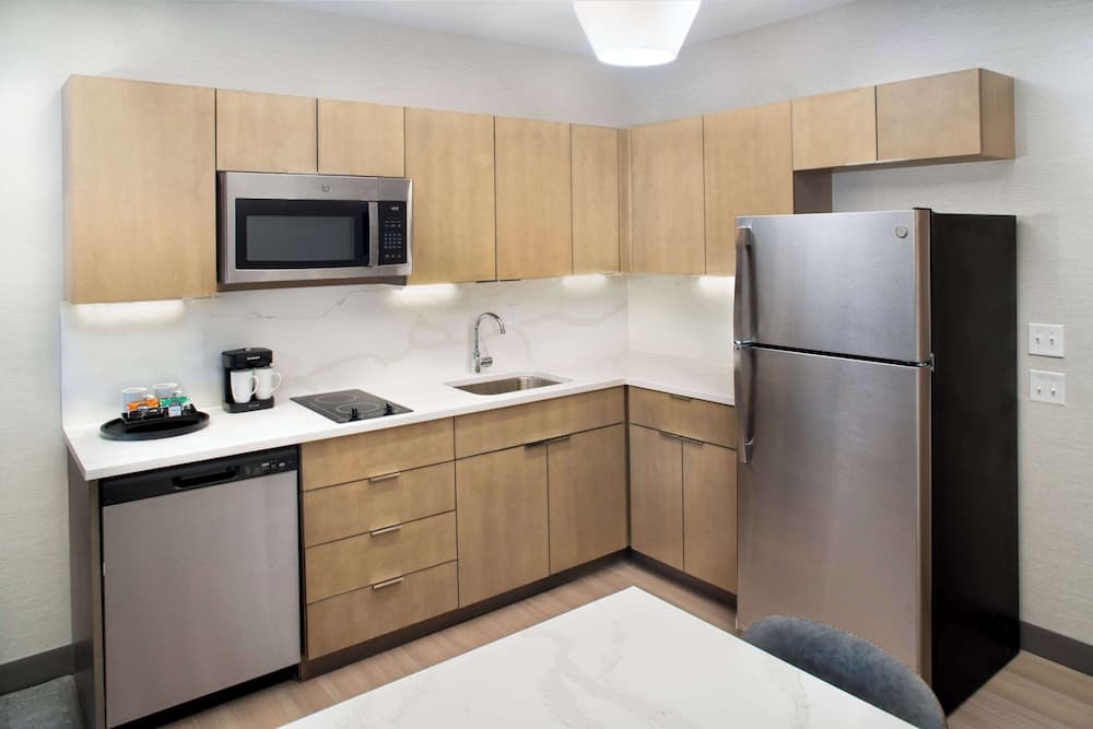A modern, compact hotel kitchenette featuring light wood cabinetry, stainless steel appliances, and a cozy dining area, ideal for travelers seeking self-catering convenience in a serene setting.