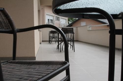 A serene rooftop terrace with black wicker chairs and tables under a glass canopy offers a cozy spot for travelers to relax and enjoy the urban view.