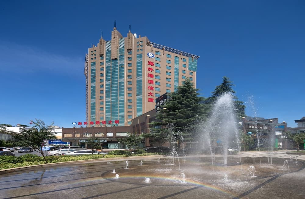A vibrant urban plaza features a lively fountain with a rainbow effect under a clear blue sky, set against the backdrop of a modern high-rise building, ideal for city exploration and photography.