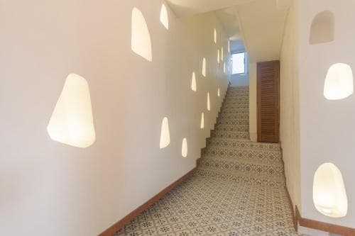A serene hotel staircase with patterned tiles, soft lighting from unique wall fixtures, and a wooden door at the top invites travelers to explore its tranquil ambiance.
