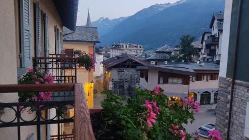 A serene evening view from a balcony adorned with pink flowers overlooks a quaint village nestled among majestic snow-capped mountains, ideal for travelers seeking peaceful alpine retreats.