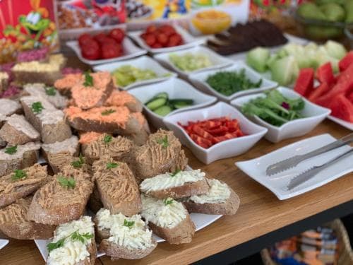 A vibrant buffet table laden with assorted spreads on bread slices, fresh vegetables, and colorful fruits creates an inviting atmosphere perfect for a catered event or group gathering.