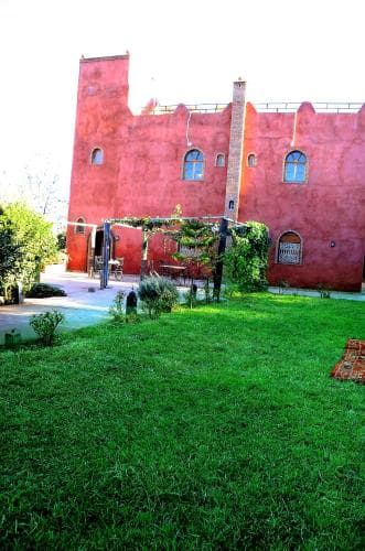 A serene courtyard with lush green grass and vibrant red walls evokes a tranquil atmosphere, perfect for travelers seeking a peaceful retreat in a historic villa setting.