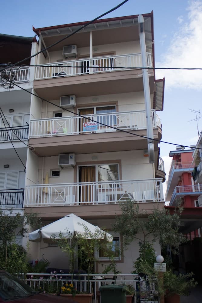 A cozy apartment building with balconies adorned by white railings and air conditioning units, surrounded by greenery and a patio umbrella, offers a serene urban retreat ideal for travelers seeking a comfortable stay in a Mediterranean setting.