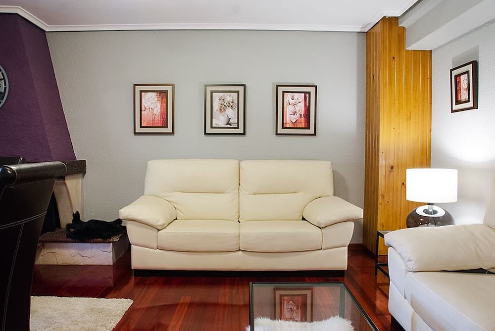 A cozy living room with a white leather sofa, framed floral artwork, wooden accents, and soft lighting creates an inviting atmosphere ideal for vacation rental seekers.