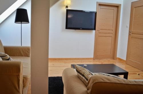 A cozy living room with beige sofas, a sleek black coffee table, and a mounted TV creates a warm and inviting atmosphere, ideal for travelers seeking comfort in a modern apartment setting.