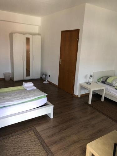 A cozy hotel room with wooden flooring, two neatly made beds, a wardrobe, and minimal decor offers a comfortable stay for travelers seeking simplicity and cleanliness.