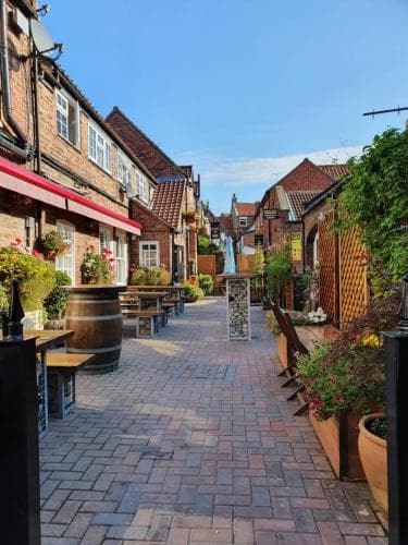 A charming cobblestone alley lined with quaint brick buildings, outdoor seating, and vibrant flower arrangements creates an inviting atmosphere perfect for leisurely strolls and exploring local eateries.
