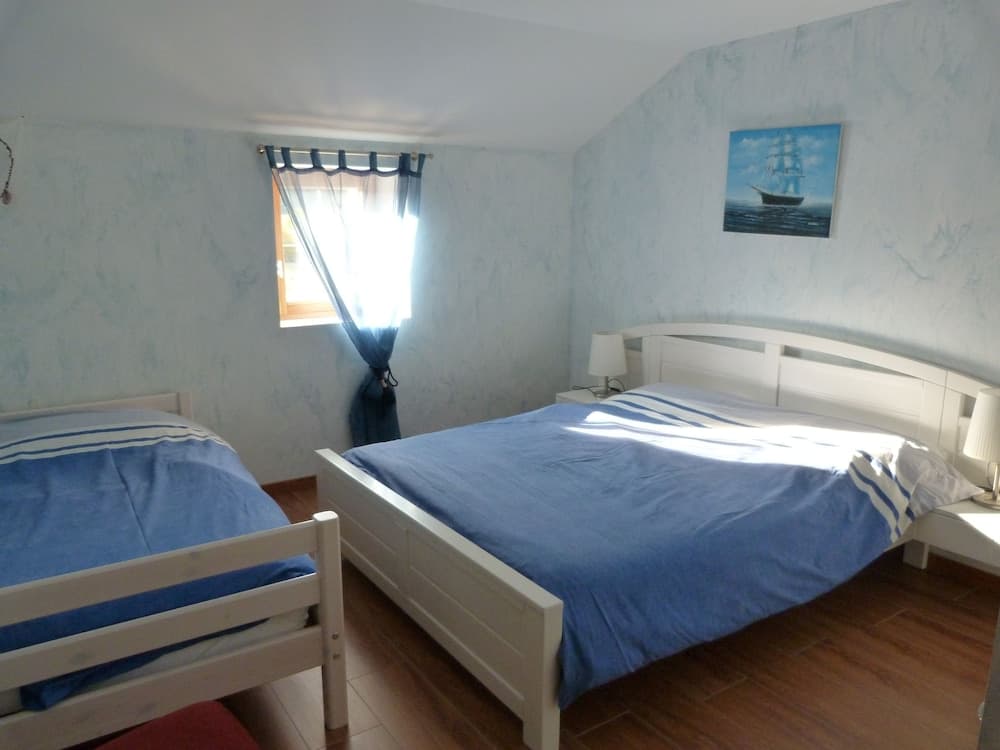 A serene coastal-themed bedroom with blue walls, white wooden beds, nautical decor, and a sunny window view, ideal for a relaxing seaside getaway.