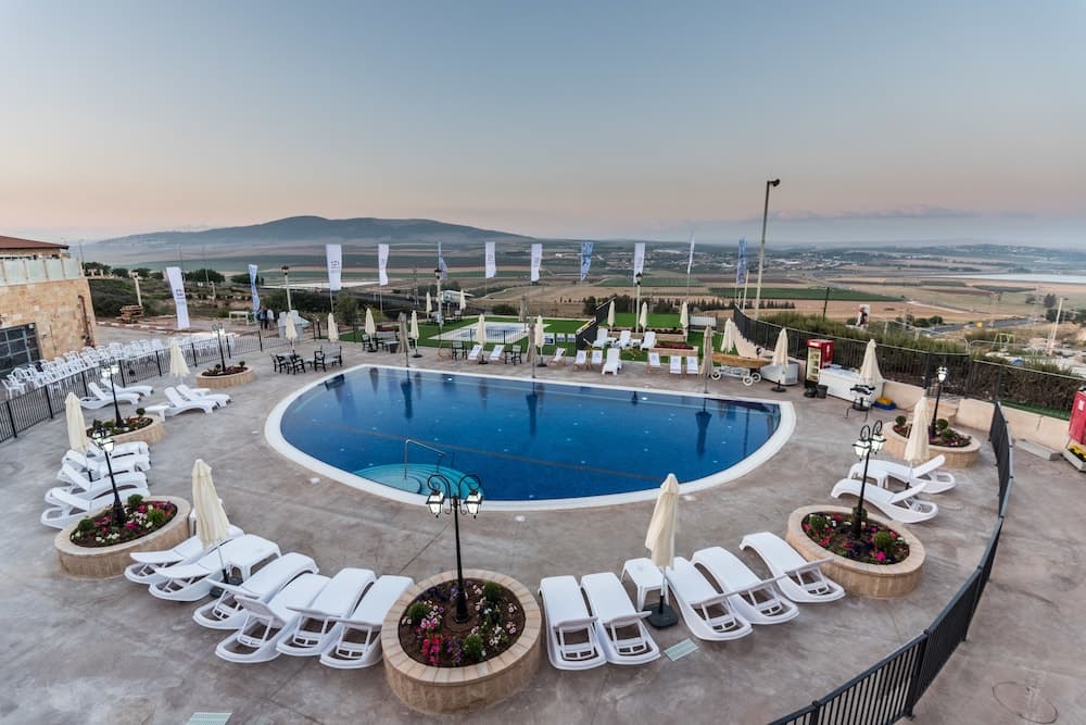 A serene rooftop pool area with lounge chairs, umbrellas, and flower beds overlooks a picturesque landscape at dusk, ideal for relaxation and leisure travel.