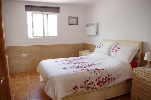 A cozy bedroom with a neatly made bed adorned with red floral bedding, tiled floors, and soft natural light from a window, ideal for travelers seeking a comfortable and serene accommodation experience.