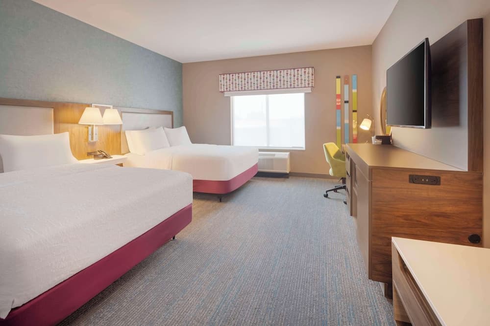 A cozy hotel room features two neatly made beds, a desk with a mounted TV, and a bright window, creating a welcoming atmosphere ideal for travelers seeking comfort and convenience.