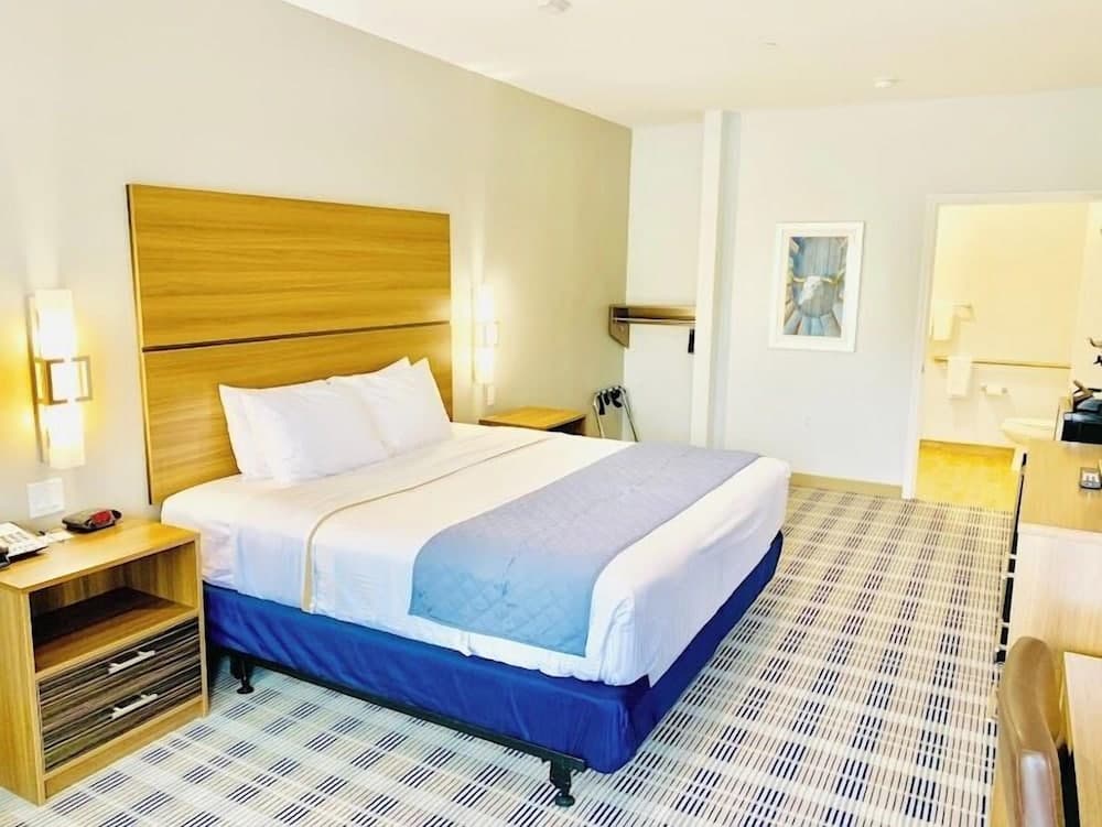 A cozy hotel room features a neatly made bed with white linens and a blue runner, wooden furnishings, warm lighting, and a patterned carpet, ideal for travelers seeking comfort and relaxation.
