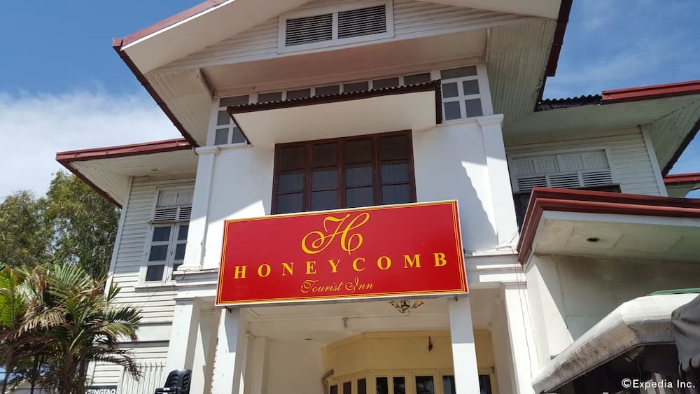A charming two-story white building with a red roof and a prominent "Honeycomb Tourist Inn" sign offers a welcoming atmosphere for travelers seeking a cozy accommodation experience amidst lush greenery.