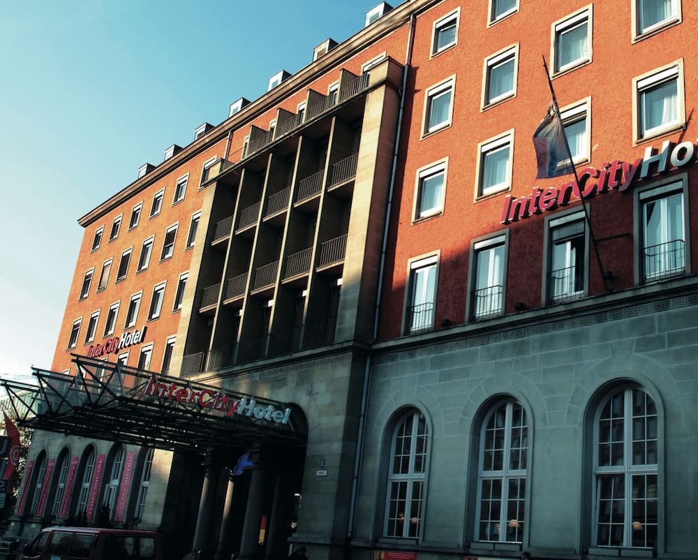 A vibrant InterCityHotel with red brick architecture, arched windows, and a modern entrance canopy stands invitingly under a clear blue sky, perfect for travelers seeking urban accommodations.