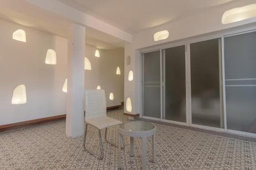 A cozy apartment interior features a patterned tiled floor, modern white furniture, and unique wall-mounted lights, creating an inviting atmosphere ideal for short-term rentals or urban living.