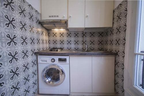 A cozy kitchenette with patterned tiles, a compact washing machine, and soft lighting creates an inviting atmosphere ideal for travelers seeking a functional and stylish short-term rental space.