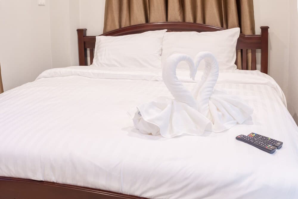 A cozy hotel room features a neatly made bed adorned with towel swans and a remote control, evoking a welcoming and comfortable atmosphere ideal for travelers seeking relaxation.