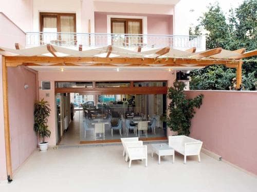 A cozy outdoor seating area with white furniture under wooden pergolas invites relaxation at a charming hotel patio, perfect for travelers seeking a serene dining or lounging spot.