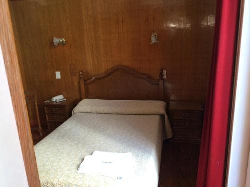 A cozy, wood-paneled bedroom with a neatly made bed, matching nightstands, and warm lighting creates an inviting atmosphere ideal for travelers seeking a comfortable and rustic retreat.