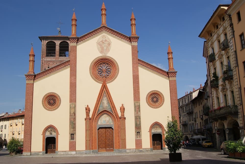 A serene European town square features a grand church with ornate brickwork, arched windows, and statues, set against a clear blue sky, ideal for cultural exploration and photography.