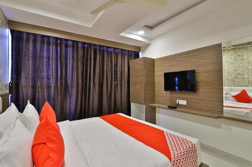 A cozy hotel room features a neatly made bed with orange accents, wooden paneling, a mounted TV, and plush curtains, ideal for travelers seeking comfort and modern amenities.