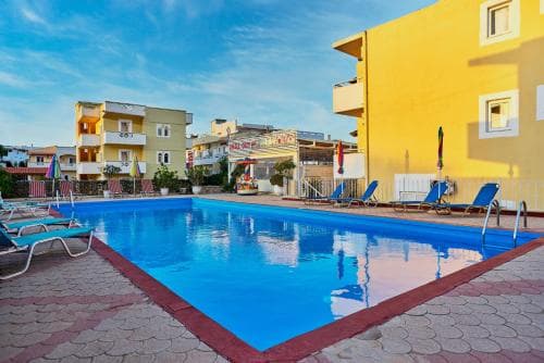 A vibrant resort pool area surrounded by colorful buildings under a clear blue sky, featuring lounge chairs and umbrellas, ideal for a relaxing vacation getaway.