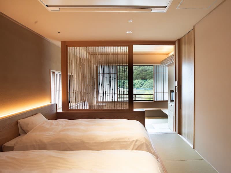 A serene Japanese ryokan room features tatami flooring, traditional sliding doors, and a tranquil view of lush greenery, ideal for travelers seeking a peaceful and authentic cultural experience in Kyoto.
