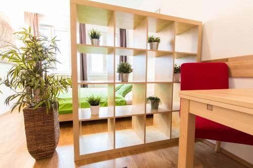 A cozy apartment interior features a wooden shelving unit adorned with potted plants, creating a serene and organized space ideal for travelers seeking comfort and functionality.