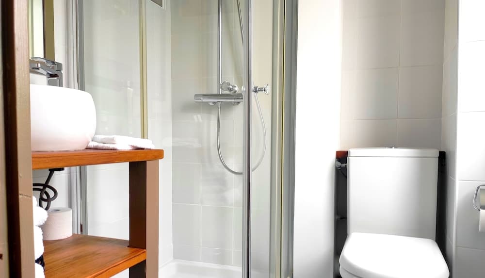 A modern, minimalist bathroom features a sleek glass shower enclosure, a wooden vanity with a white sink, and a clean toilet, ideal for travelers seeking comfort and style in their accommodations.