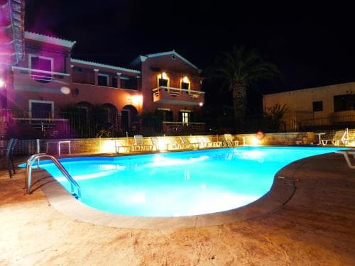 A serene night scene at a resort featuring a brightly lit pool surrounded by lounge chairs, palm trees, and warmly illuminated buildings, ideal for travelers seeking relaxation and leisure.