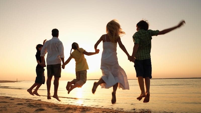 A joyful family leaps hand-in-hand on a serene beach at sunset, capturing the essence of a perfect vacation moment ideal for travelers seeking family-friendly destinations near airports like Leknes Lufthavn in Norway.