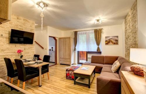 A cozy living room with wooden floors, stone walls, and modern furnishings creates a warm and inviting atmosphere, perfect for travelers seeking comfort in a vacation rental.