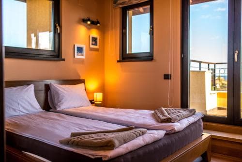 A cozy hotel room with warm lighting, neatly arranged bedding, and a balcony view of the sea, ideal for travelers seeking relaxation and comfort.
