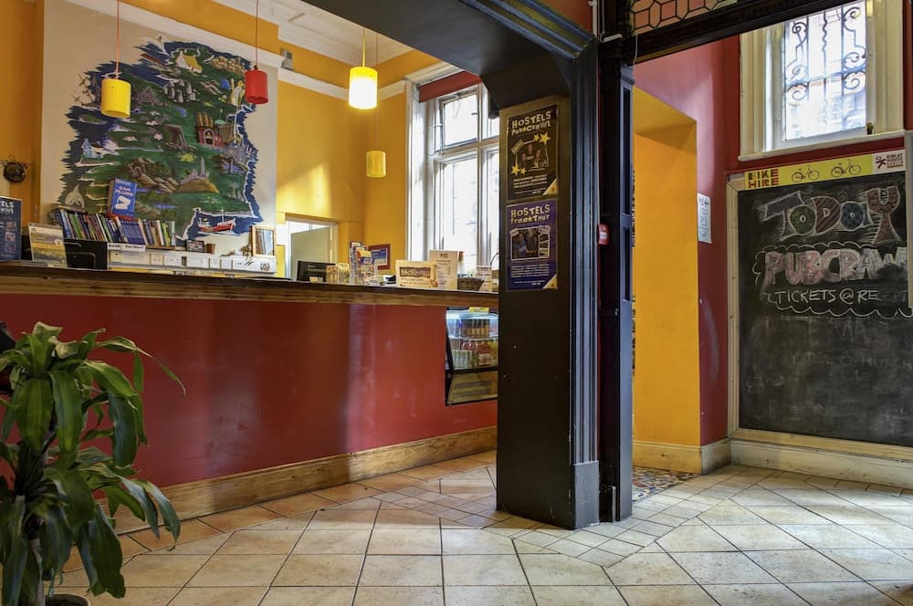 A cozy hostel lobby with vibrant yellow walls, a colorful mural, tiled floors, and a chalkboard advertising pub crawls creates an inviting atmosphere for travelers seeking local experiences.