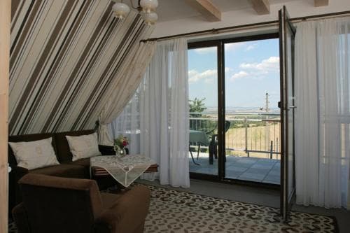 A cozy attic room with striped curtains opens to a serene balcony overlooking a vast landscape, perfect for a tranquil getaway or romantic retreat.